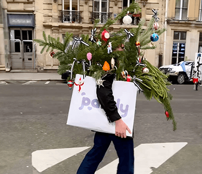 Person som bär en julgran och en Pandy-kasse över gatan